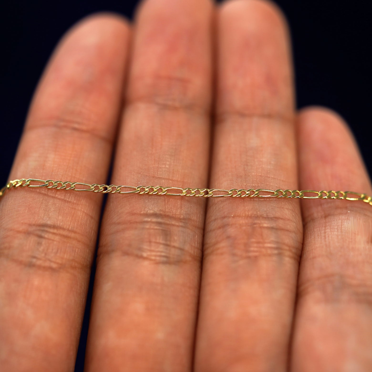 A yellow gold Figaro Chain resting on a model's fingers