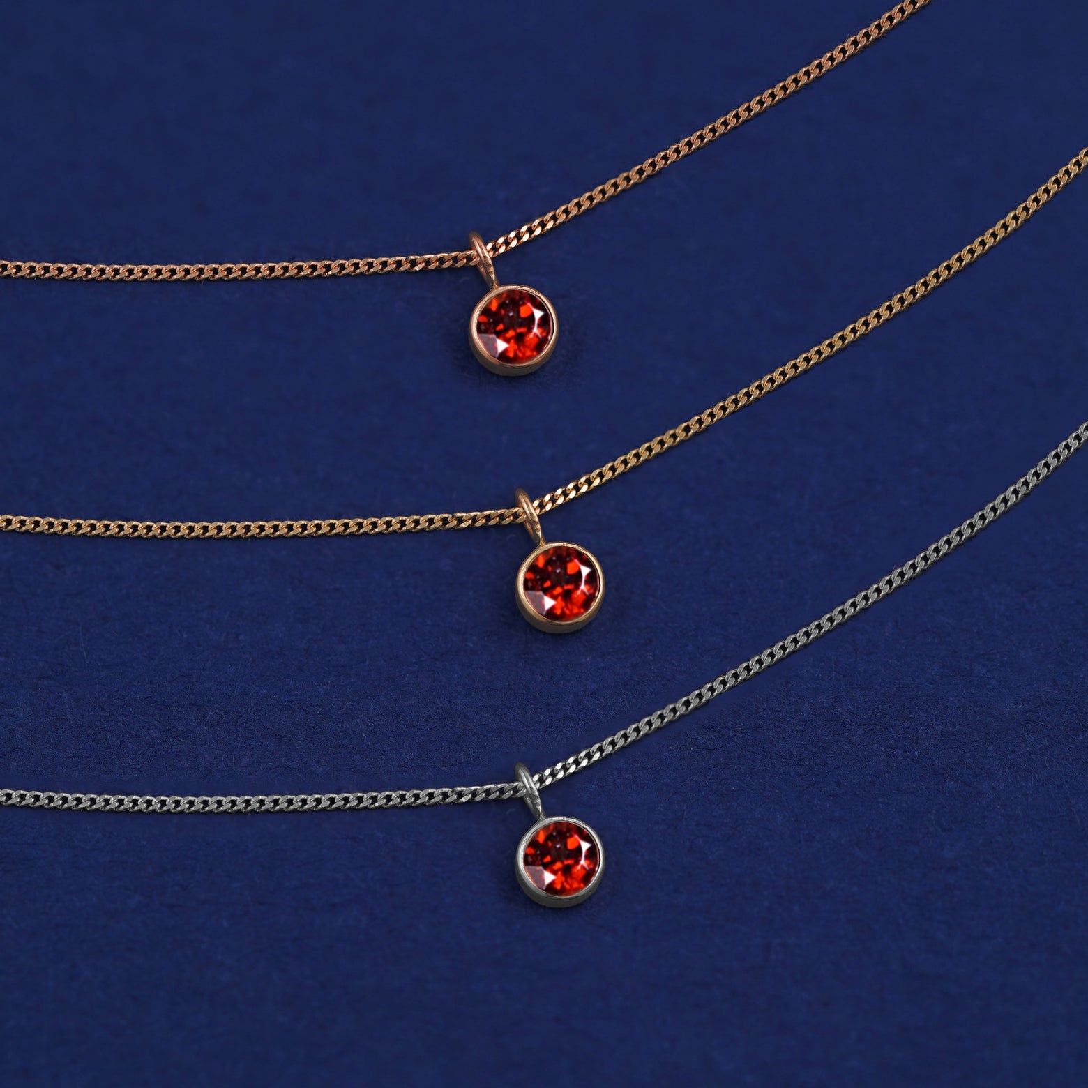 Three versions of the Garnet Necklace shown in options of yellow, white and rose gold on a dark blue background