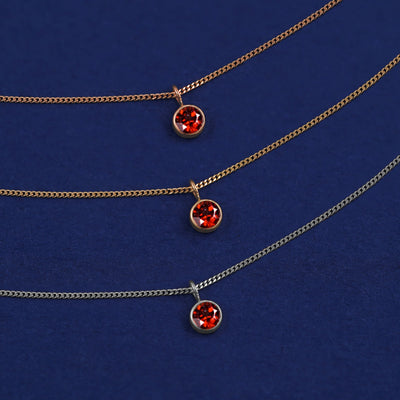 Three versions of the Garnet Necklace shown in options of yellow, white and rose gold on a dark blue background