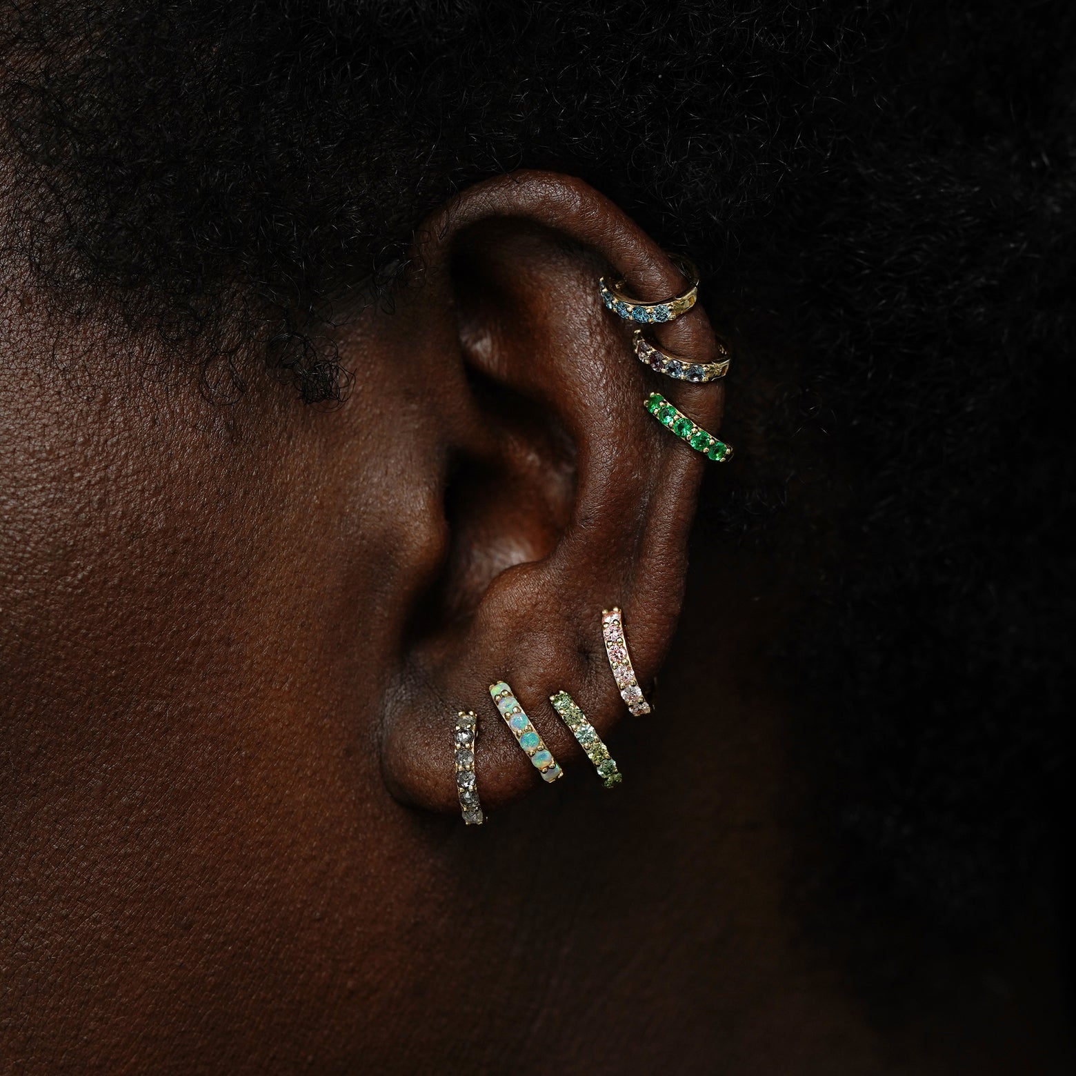 A model wearing multiple gemstone huggie hoops in several lobe and cartilage piercings
