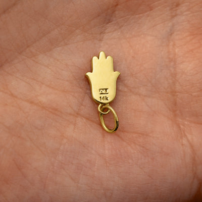Back view of a solid 14k yellow gold Hamsa Charm resting on in the palm of a model's hand