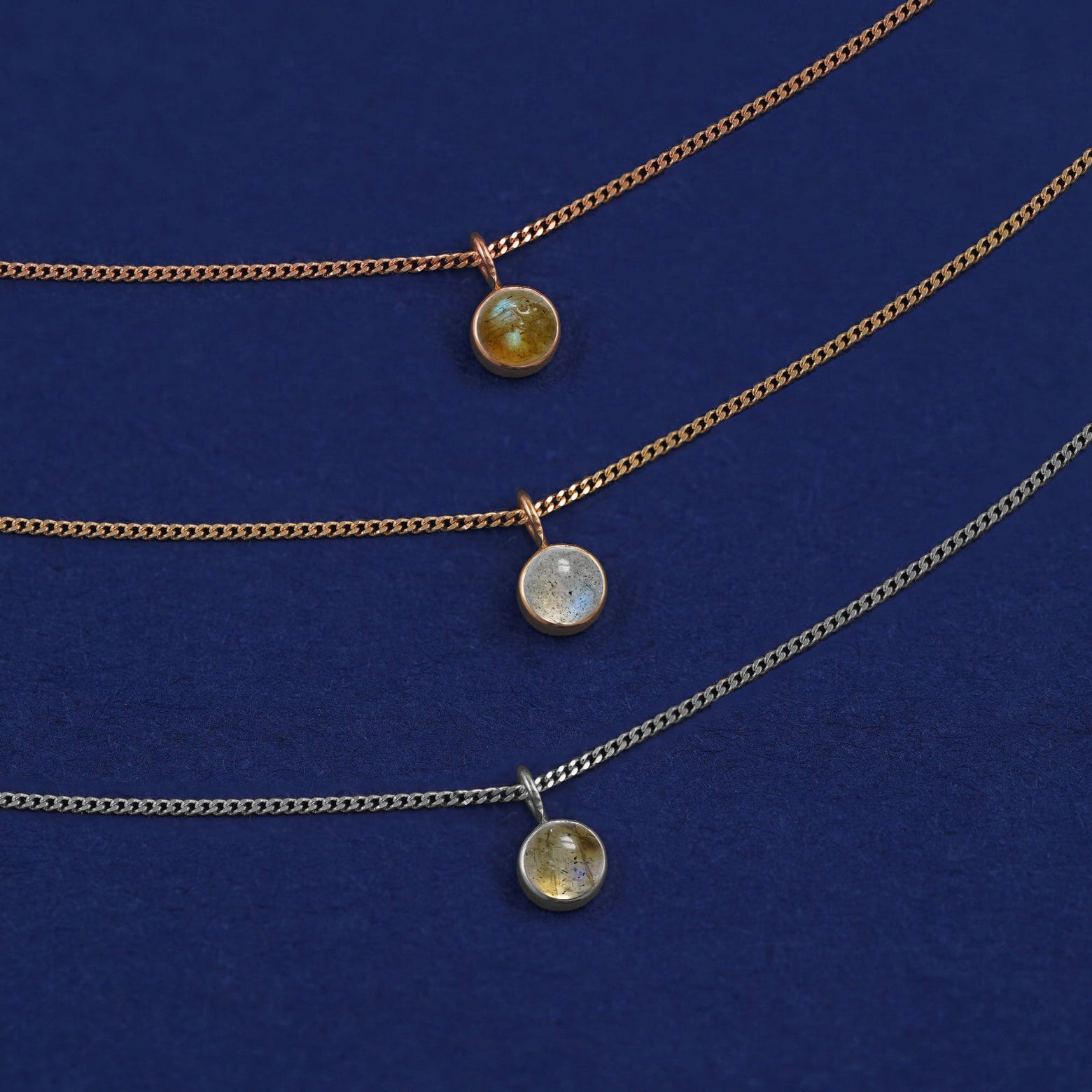 Three versions of the Labradorite Necklace shown in options of yellow, white and rose gold on a dark blue background