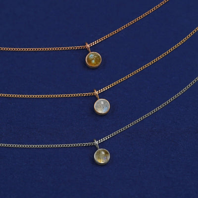 Three versions of the Labradorite Necklace shown in options of yellow, white and rose gold on a dark blue background