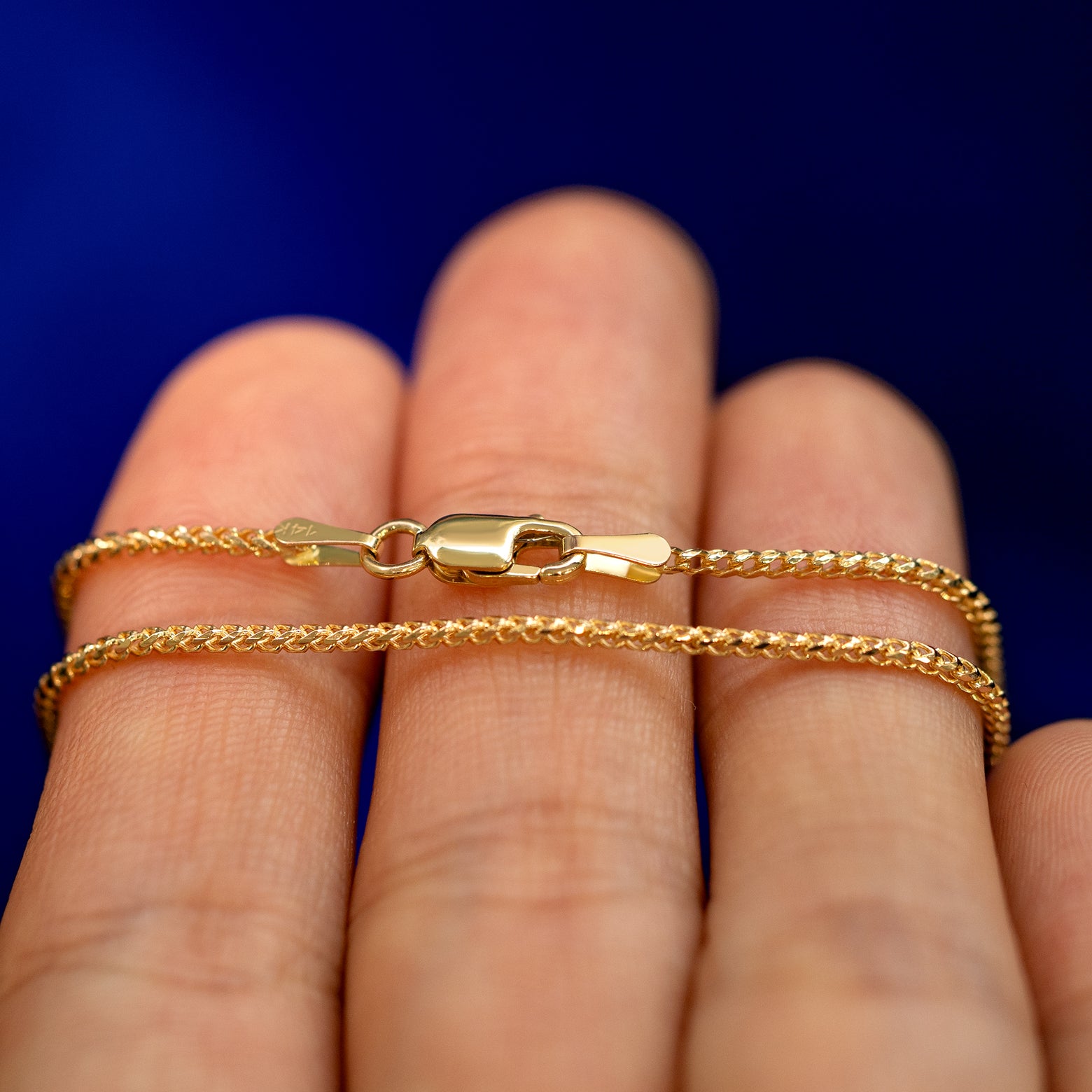 A yellow gold Mini Franco Chain Necklace wrapped around a model's fingers to show the chain and the lobster claw clasp