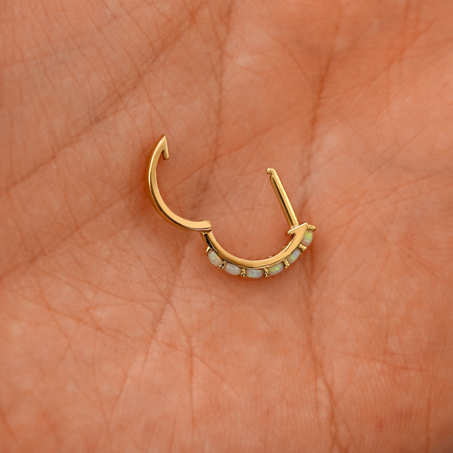 An open Opal huggie hoop laying in a models palm