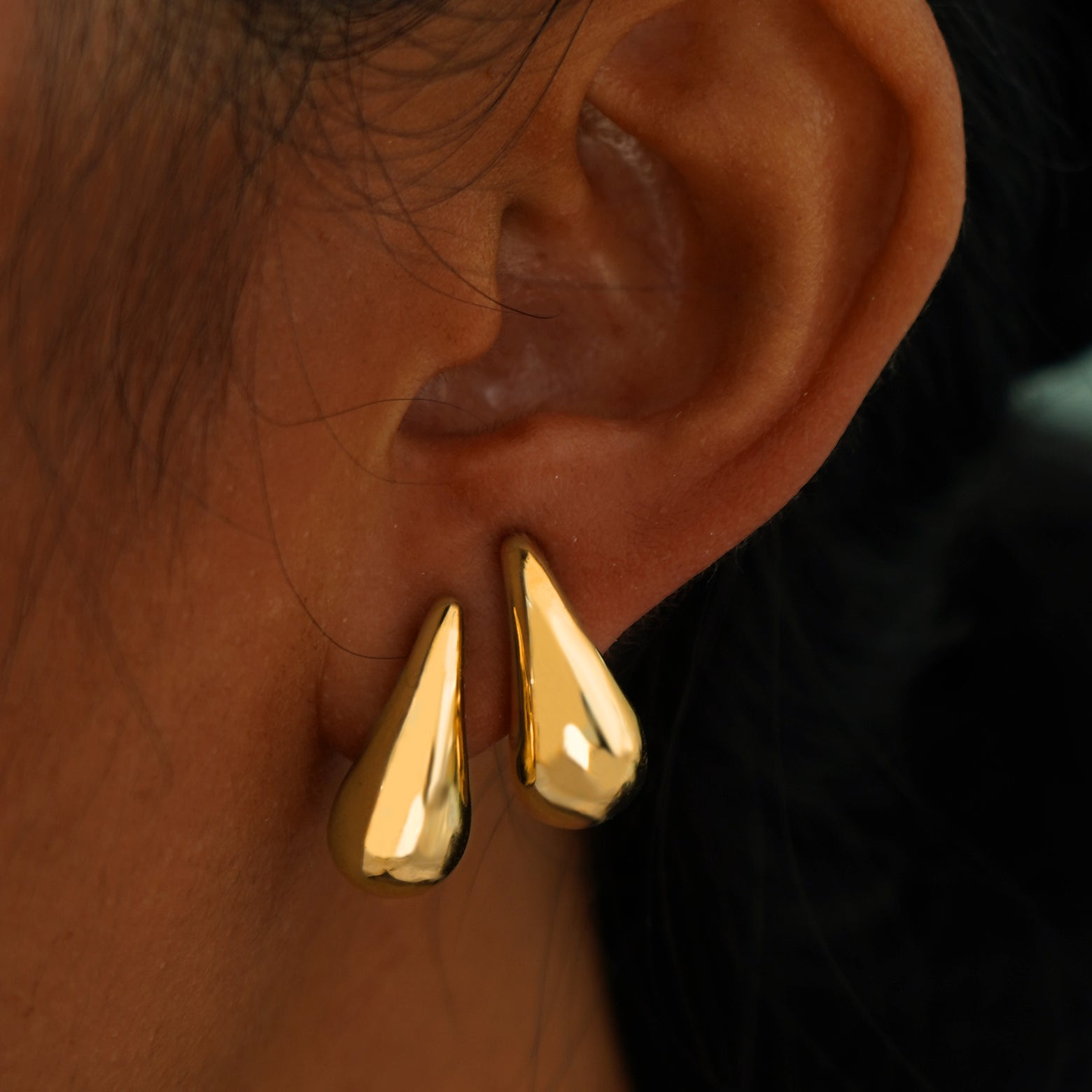 A model's ear wearing two yellow gold Teardrop Puffy Earrings in two separate lobe piercings