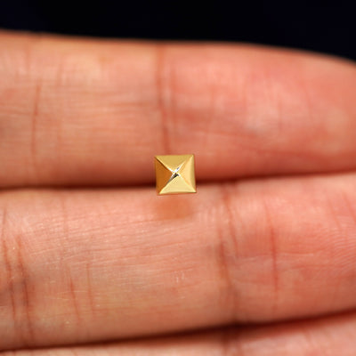A solid 14k yellow gold Pyramid Earring in between a model's fingers