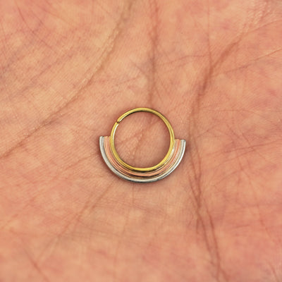 A model's hand holding a 14 karat yellow gold Pierced Rainbow Septum