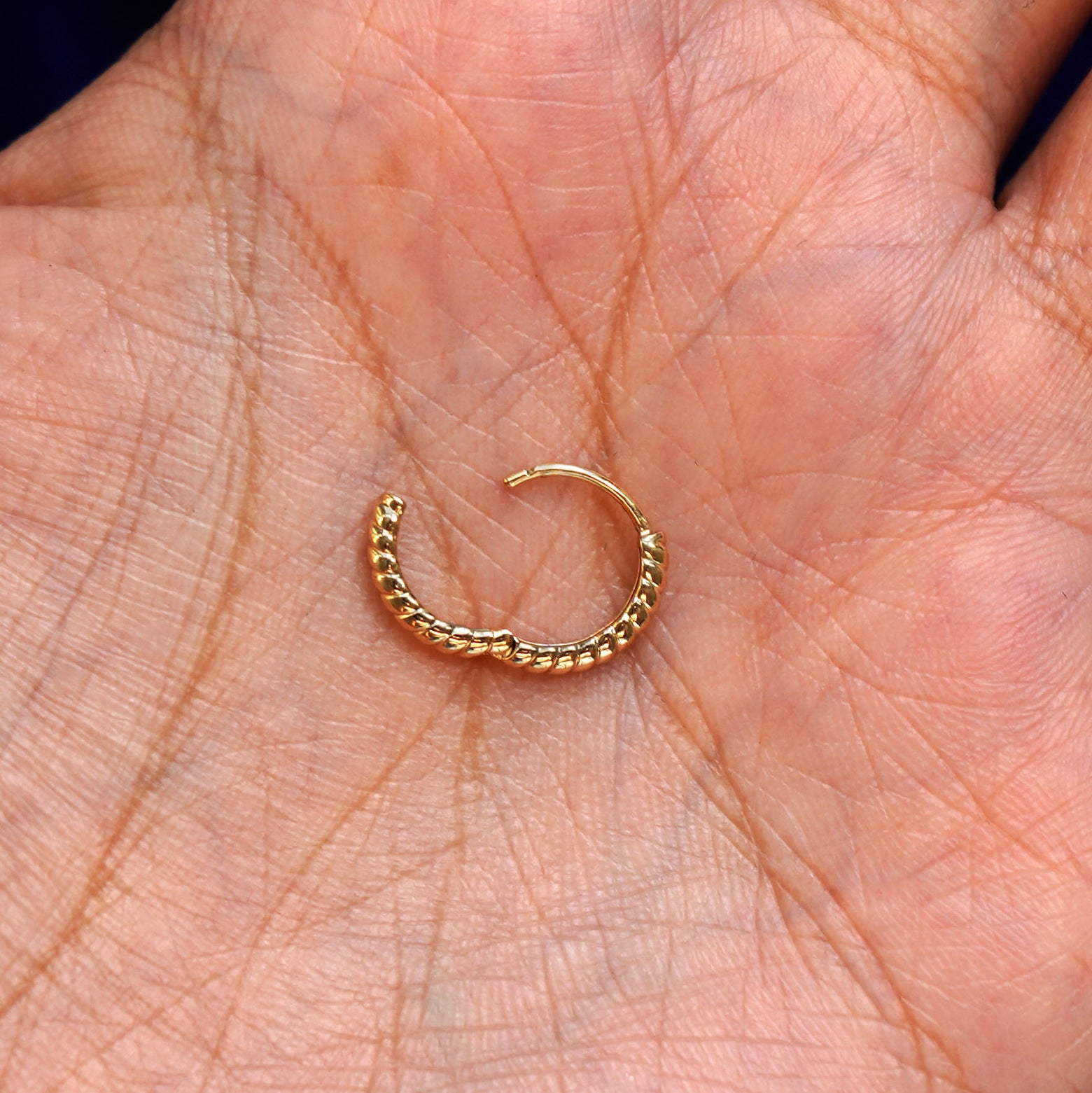 A solid 14k yellow gold Small Rope Huggie Hoop Earring open in a model's palm to show the hinge