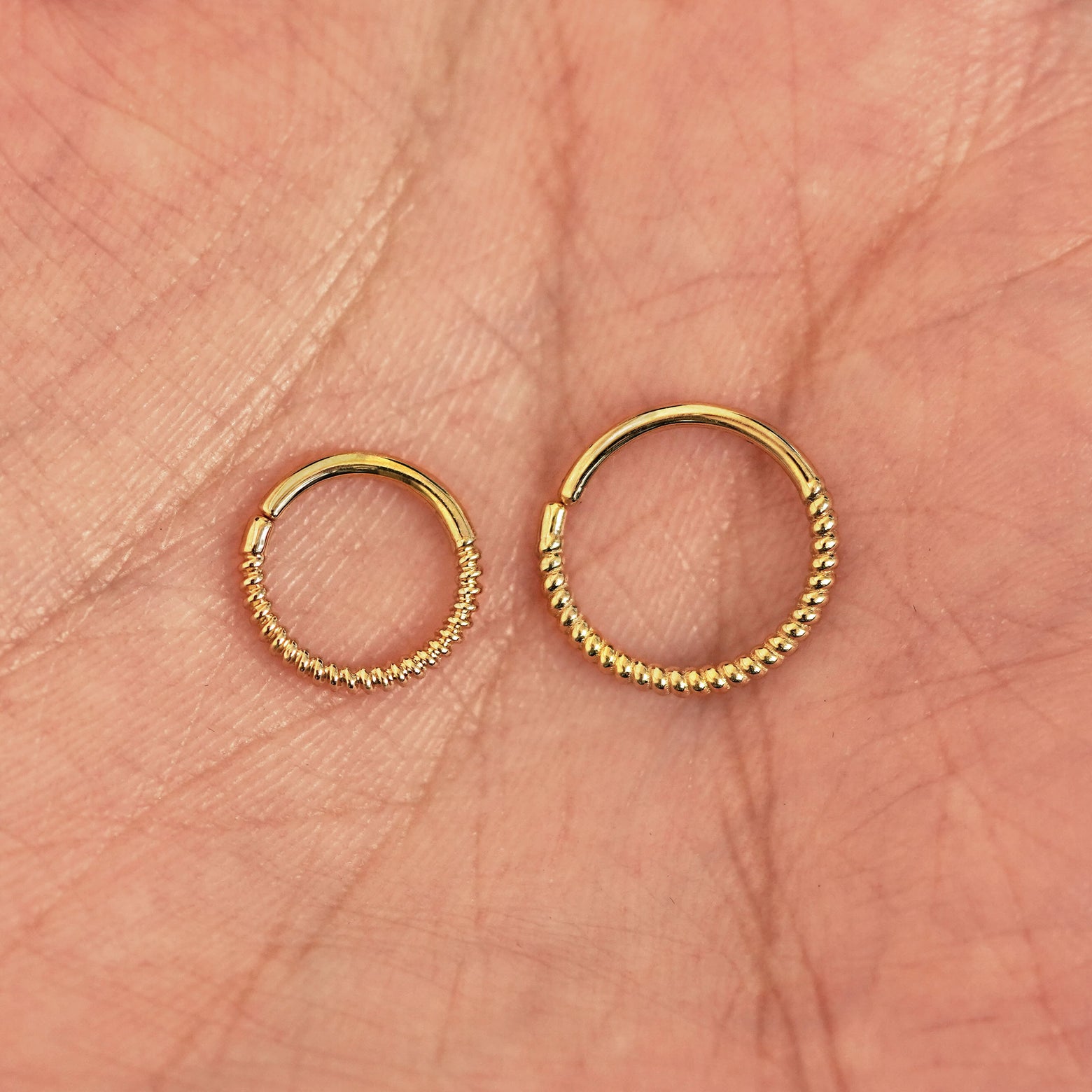 A model's palm holding two versions of the pierced Rope Septum showing the 8mm and 10mm sizes