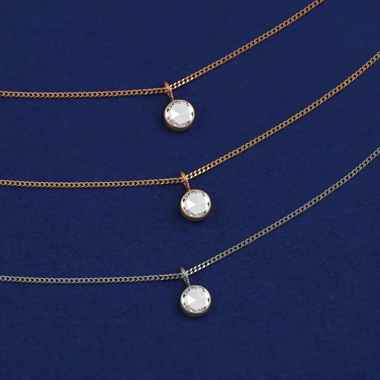 Three versions of the Rose Cut Diamond Necklace shown in options of yellow, white and rose gold on a dark blue background