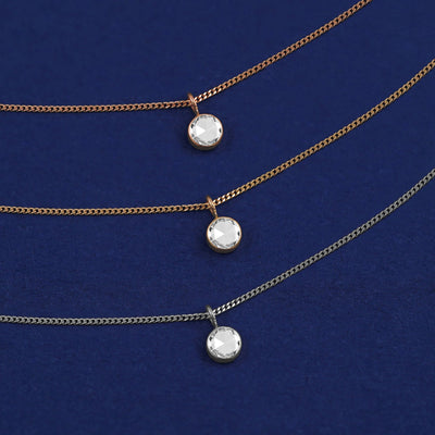 Three versions of the Rose Cut Diamond Necklace shown in options of yellow, white and rose gold on a dark blue background
