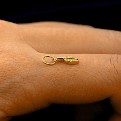 Side view of a 14k solid gold Leaf Charm on a model's finger to show the details and thickness of the charm