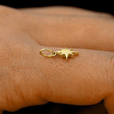 Side view of a 14k solid gold Starburst Charm on a model's finger to show the details and thickness of the charm