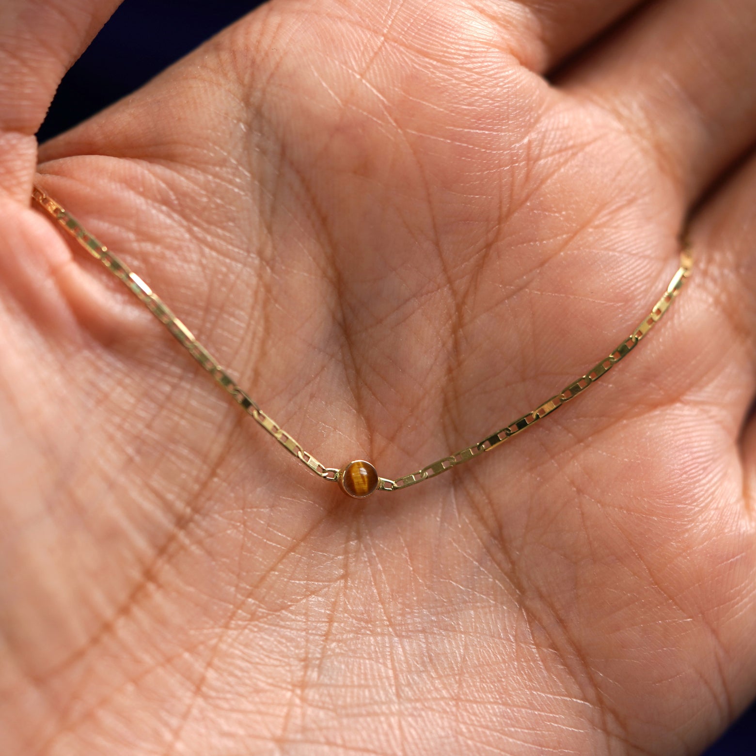 A yellow gold Tiger Eye Bracelet draped on a model's palm