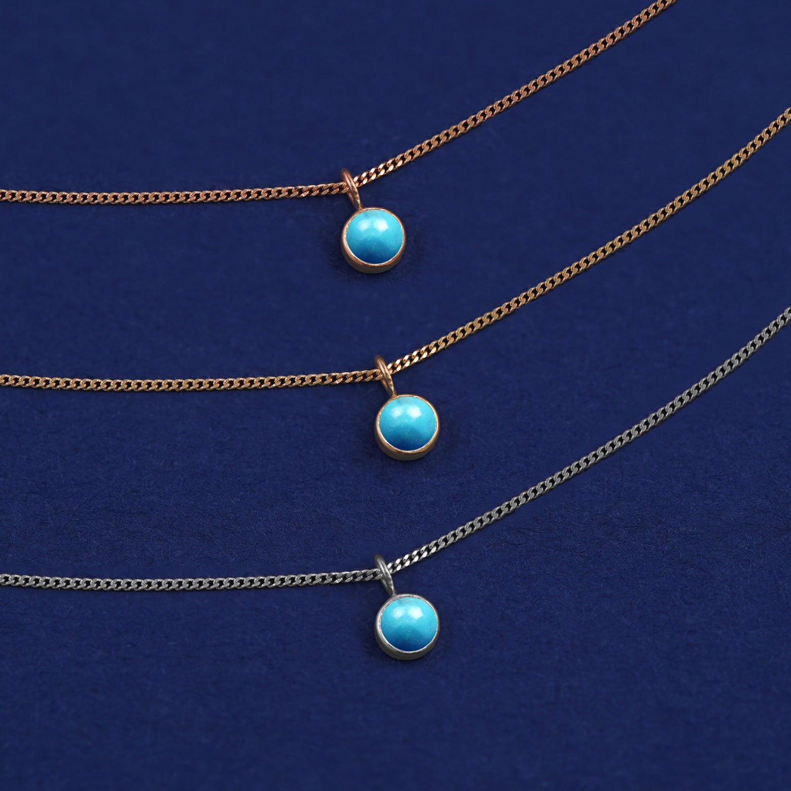 Three versions of the Turquoise Necklace in options of yellow, white, and rose gold on a dark blue background