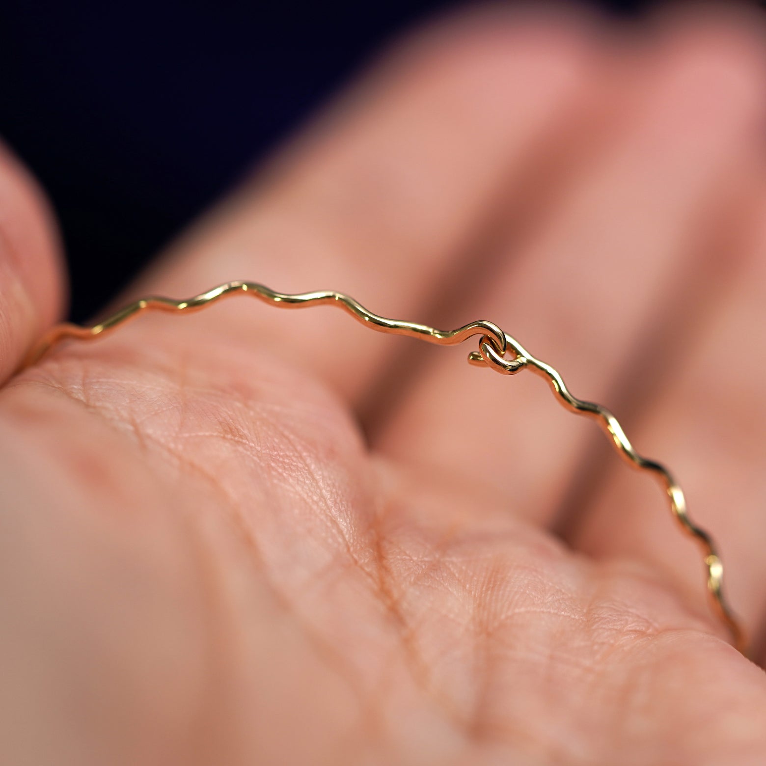 Alternate view of a model holding a 14k yellow gold Wave Bangle Bracelet to show the easy hook clasp