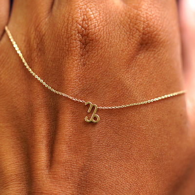 A solid gold Capricorn Horoscope Necklace resting on the back of a model's hand