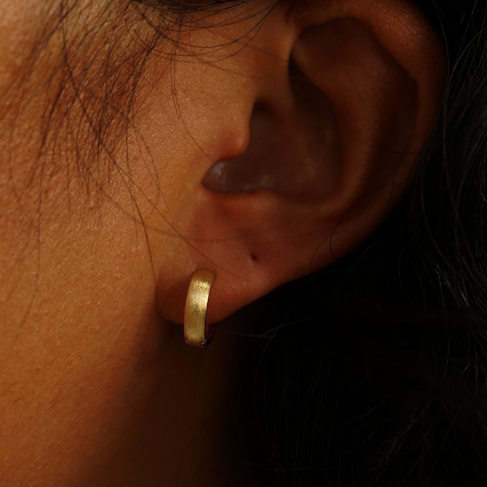 A model's ear wearing a 14k yellow gold Stardust Small Wide Huggie Hoops