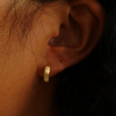 A model's ear wearing a 14k yellow gold Stardust Small Wide Huggie Hoops
