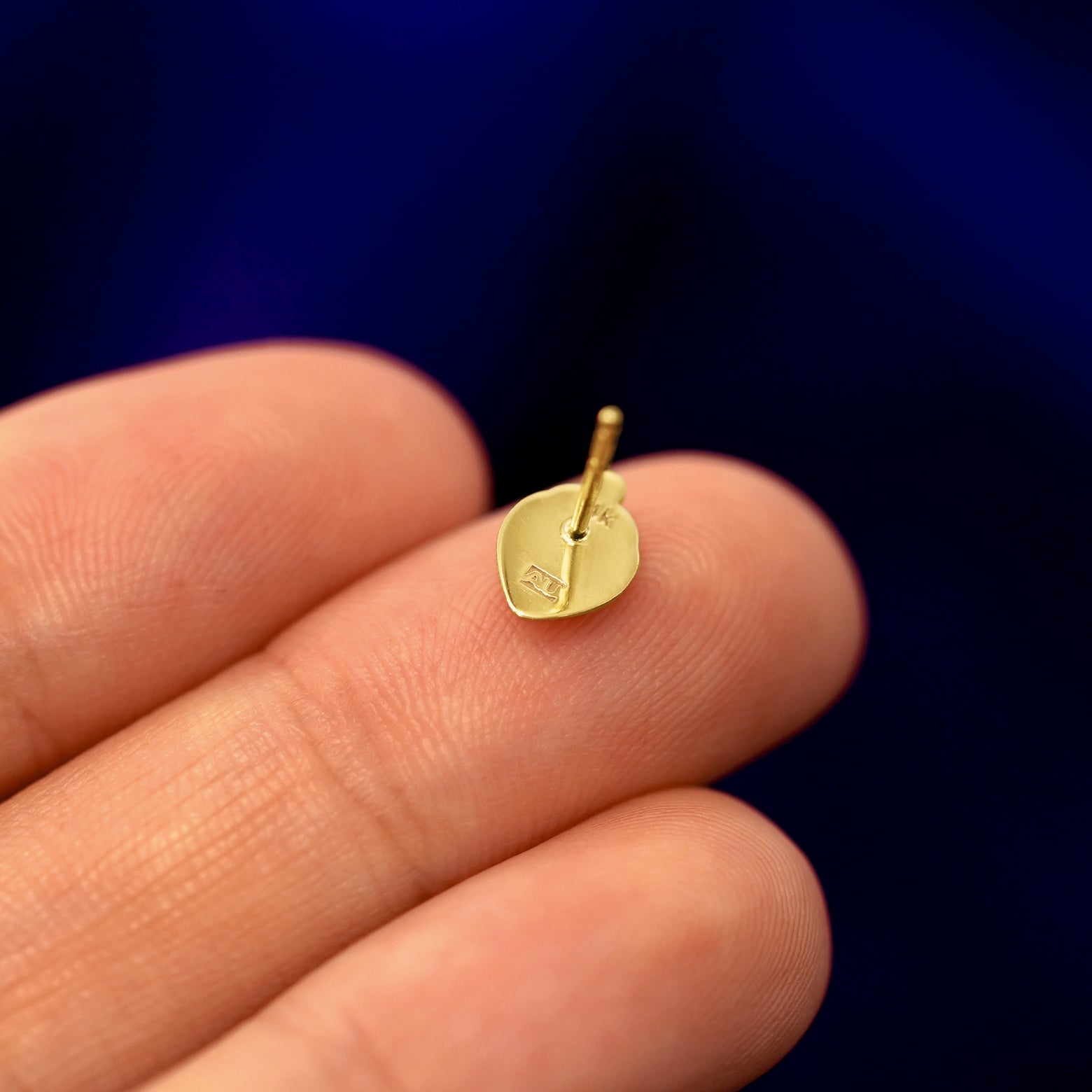 A 14k gold Strawberry Earring in a model's hand resting on its face to show the back of the stud and the post