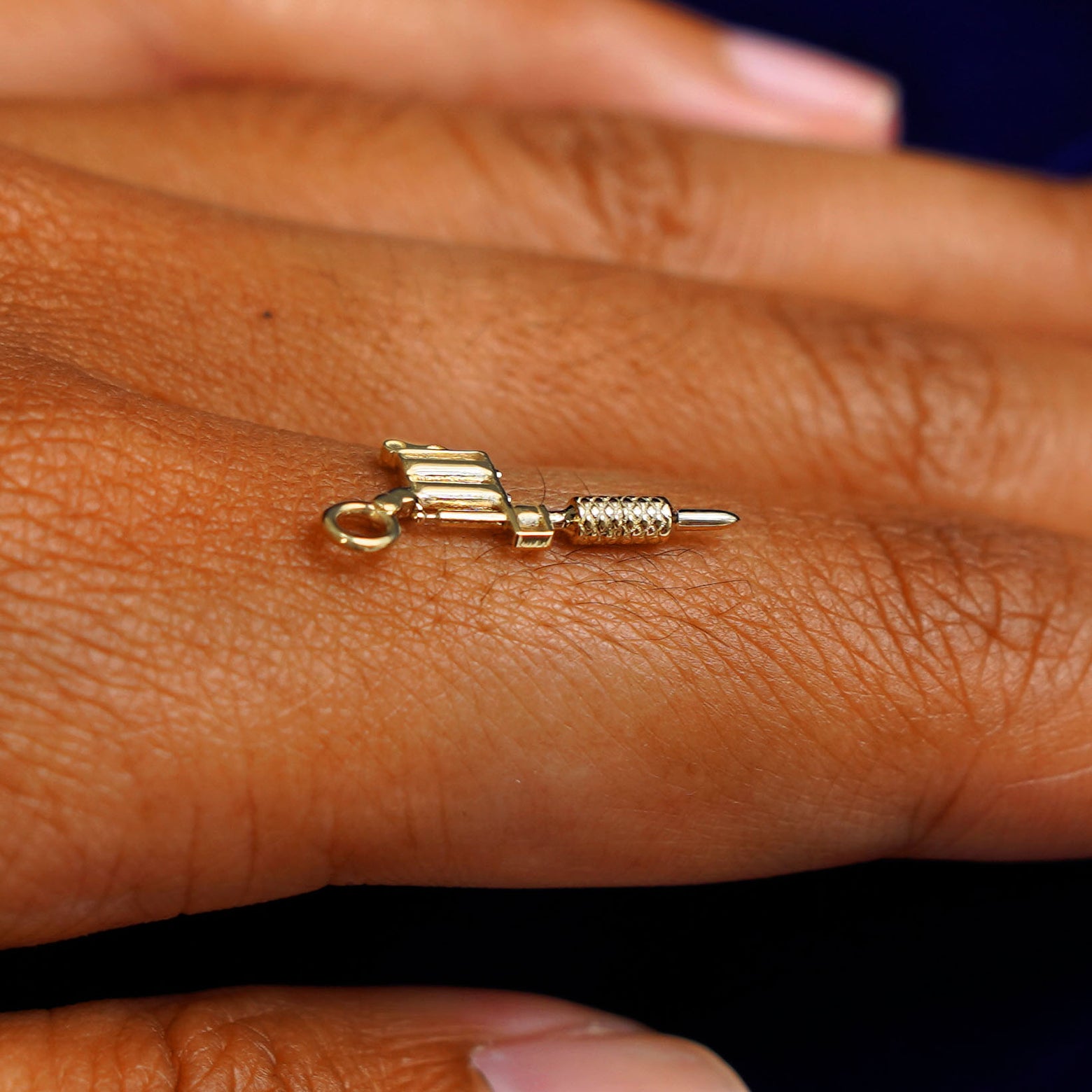 A 14k yellow gold Tattoo Machine Charm for earring balancing on the back of a model's finger