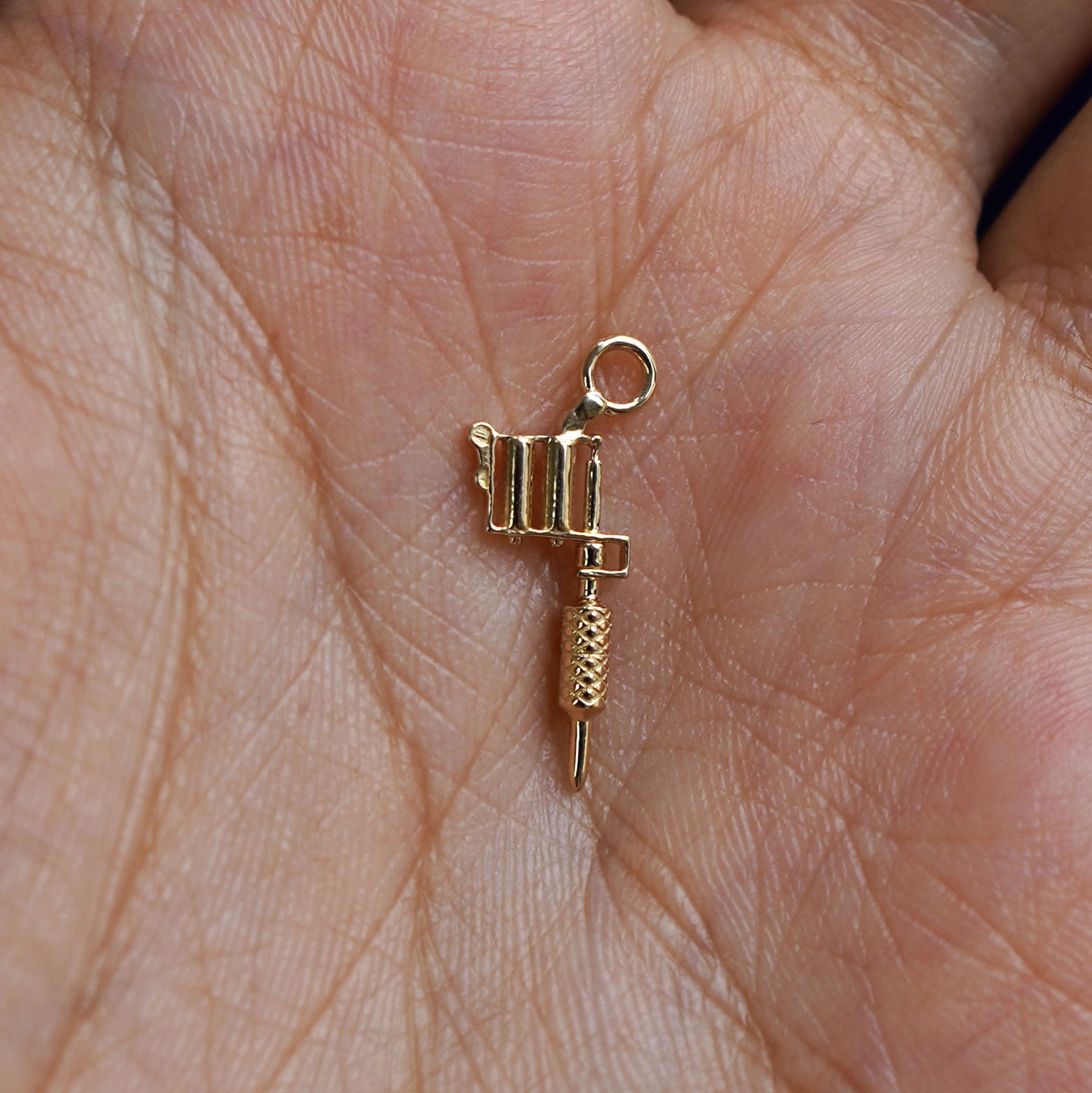 A 14k gold Tattoo Machine Charm for earring resting in a model's palm to show the underside of the charm