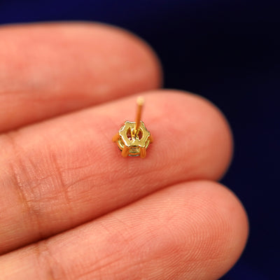 A yellow gold teal Montana Sapphire stud laying facedown on a model's fingers to show the underside view