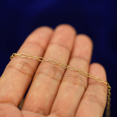A yellow gold Veren Anklet resting on a model's fingers