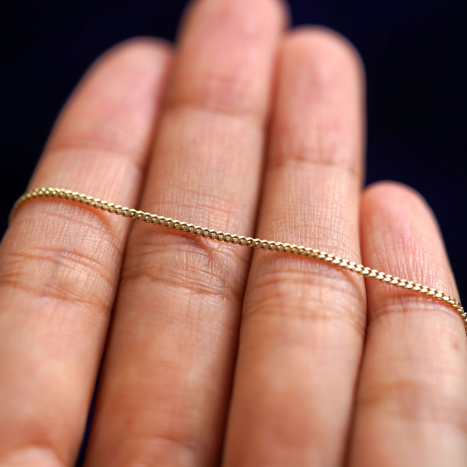 A yellow gold Mini Miami Chain resting on a model's fingers