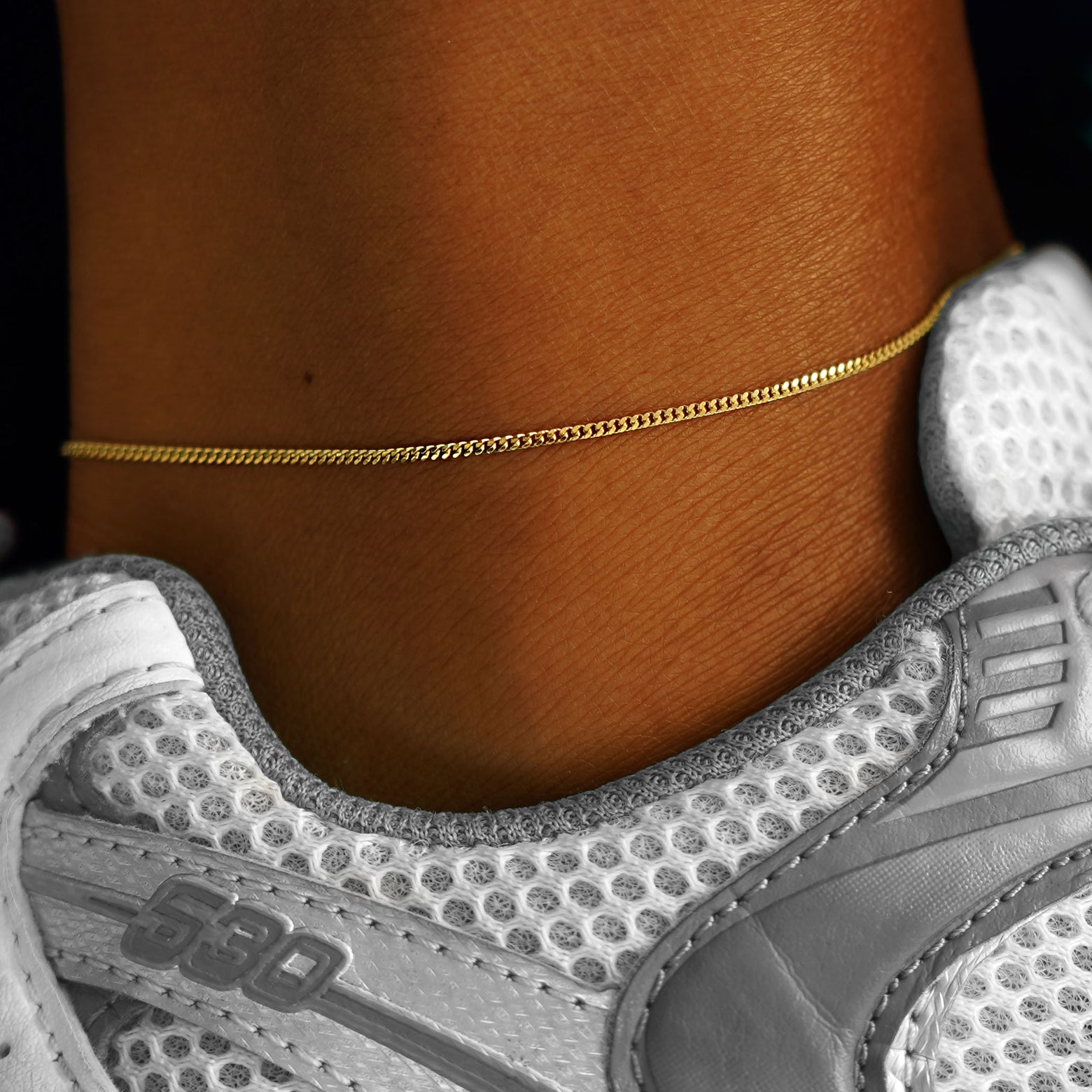 A model's ankle wearing a solid yellow gold Mini Miami Anklet