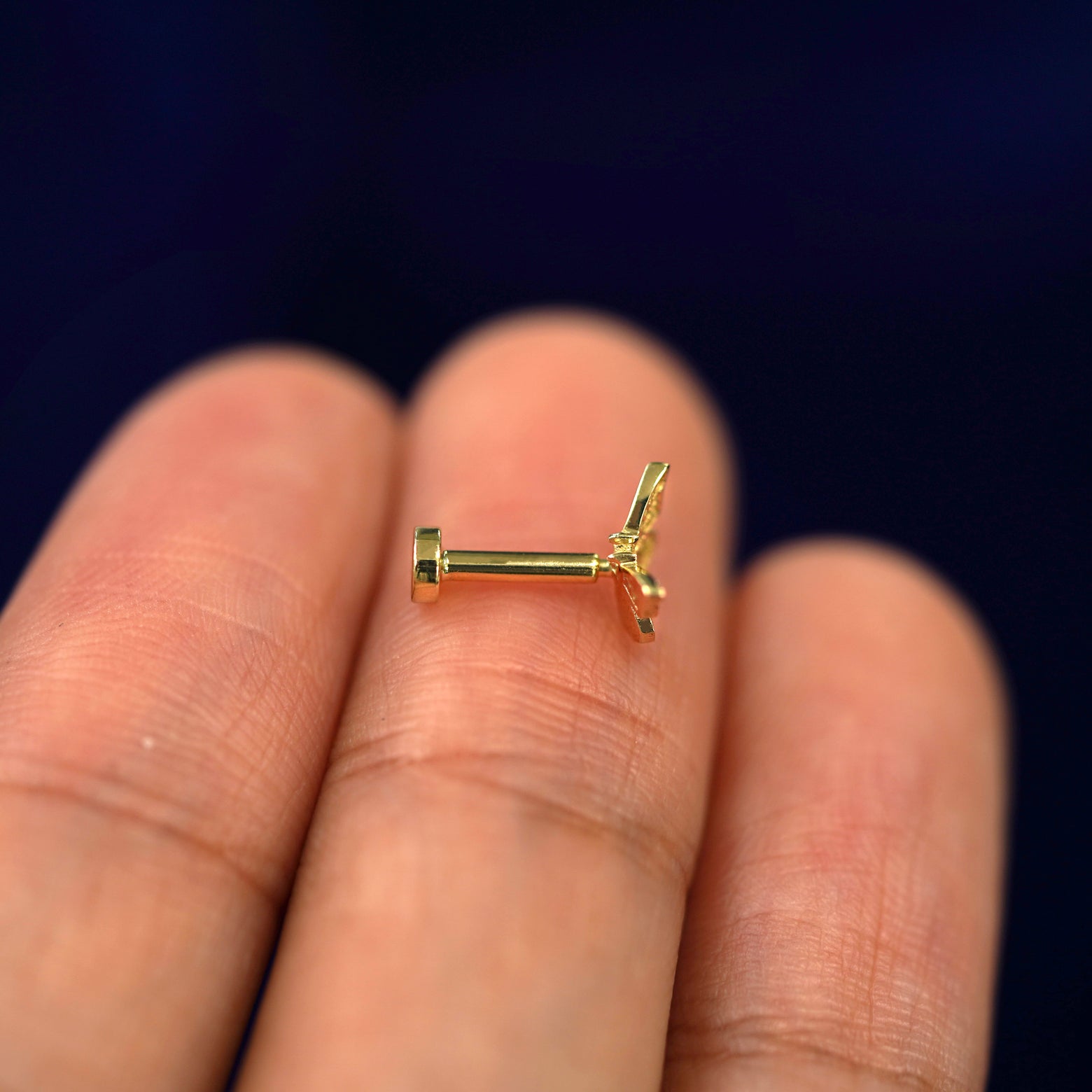 Side view of a Mini Butterfly Flat back piercing sitting on a model's fingertips