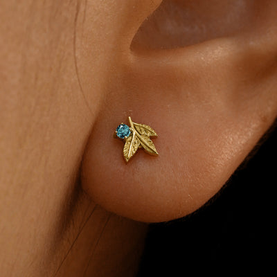 Close up view of a model's ear wearing a 14k yellow gold blue topaz 3 Leaves Gemstone Earring