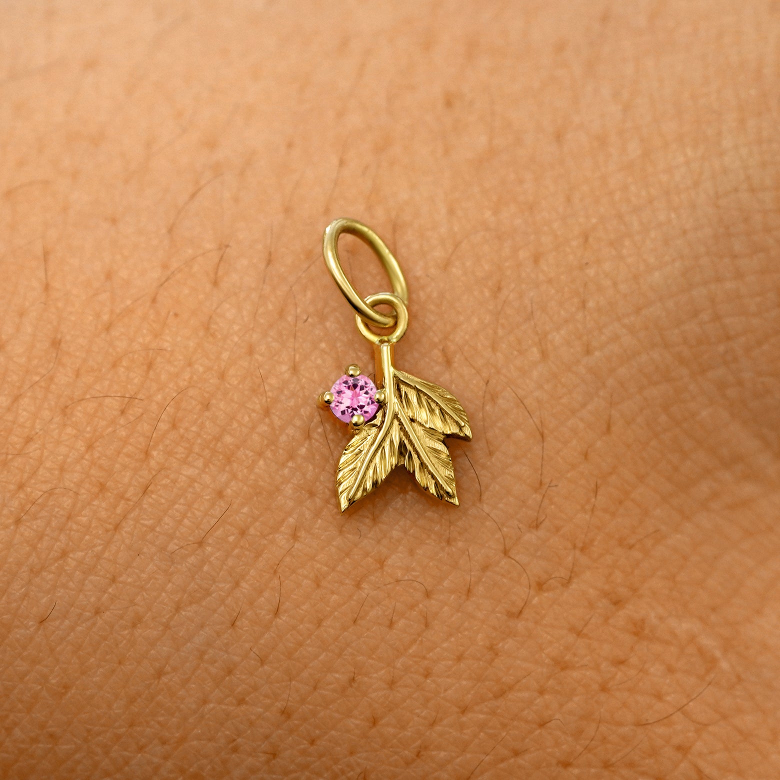 A solid 14k yellow gold pink tourmaline Gemstone 3 Leaves Charm resting on the back of a model's hand