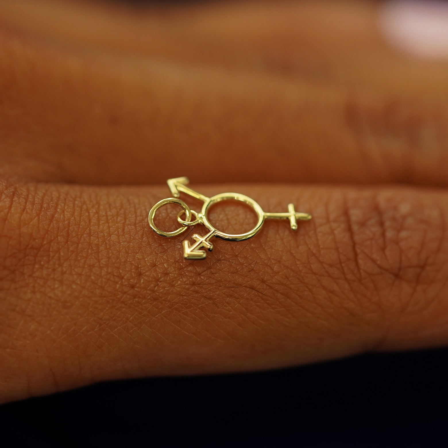 A 14k solid gold Trans Symbol Charm for chain balancing on the back of a model's finger
