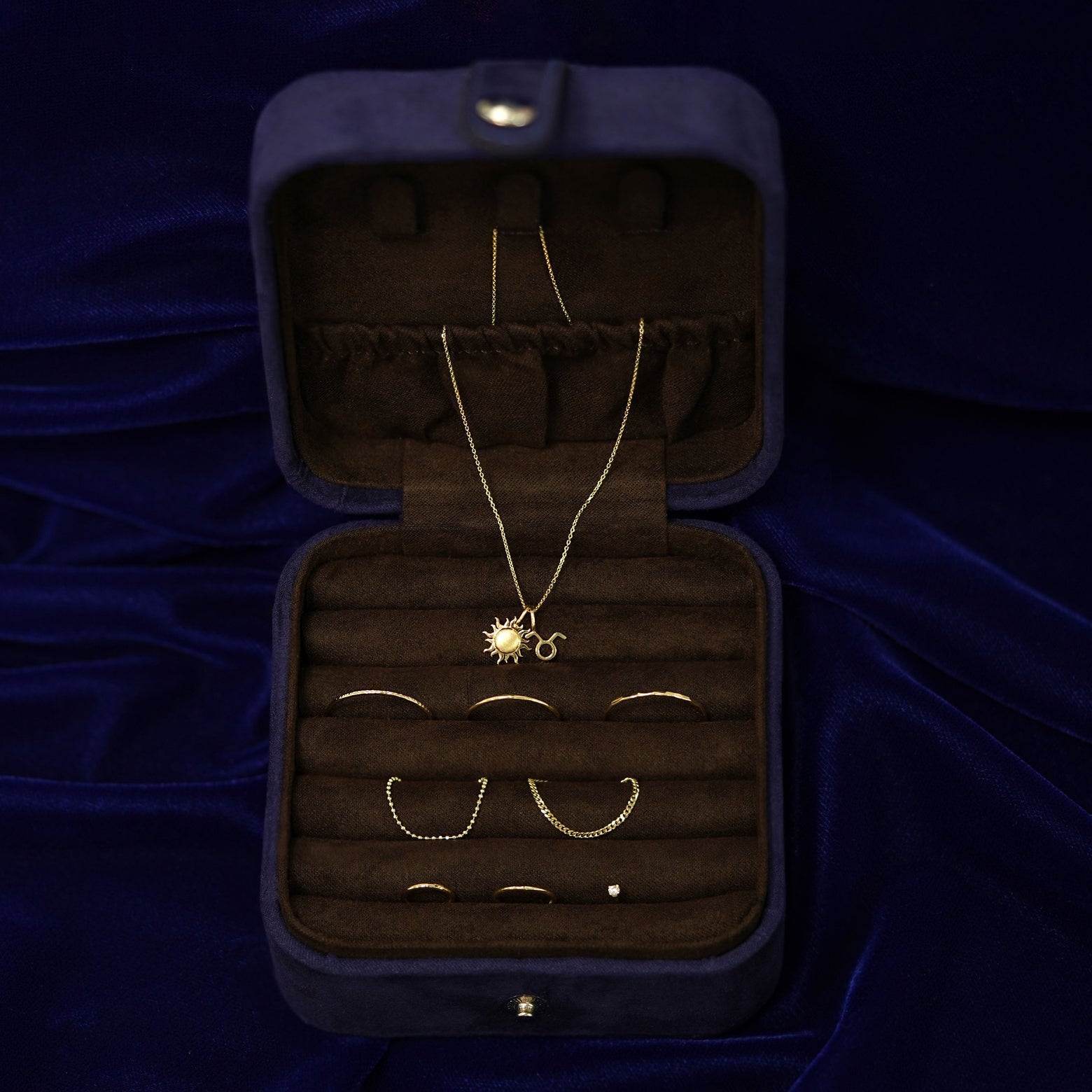 An open Automic Gold Travel Case  with multiple pieces of solid gold jewelry inside and a necklace half in the pouch on top