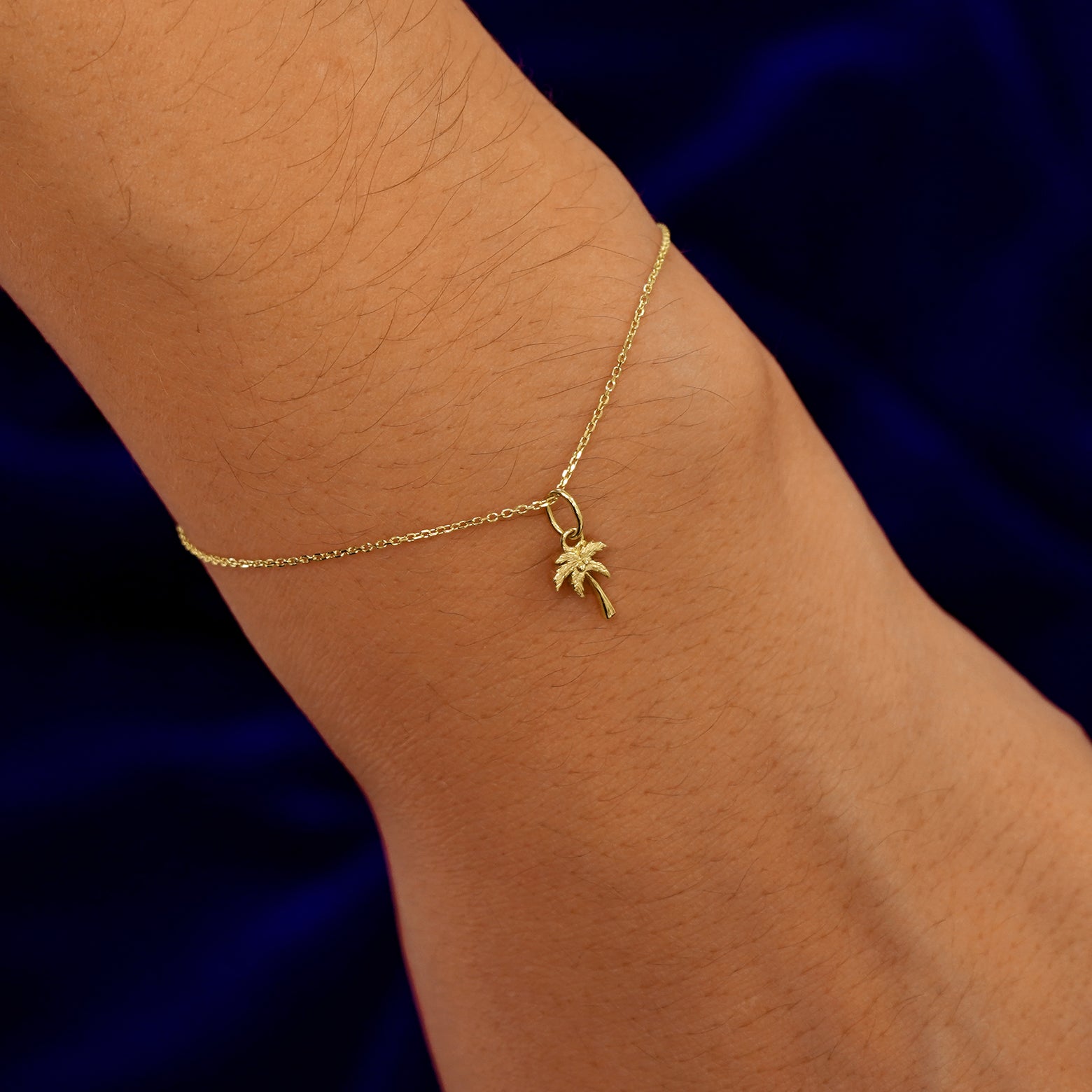 A model's wrist wearing a yellow gold Palm Tree Charm on a Cable Bracelet