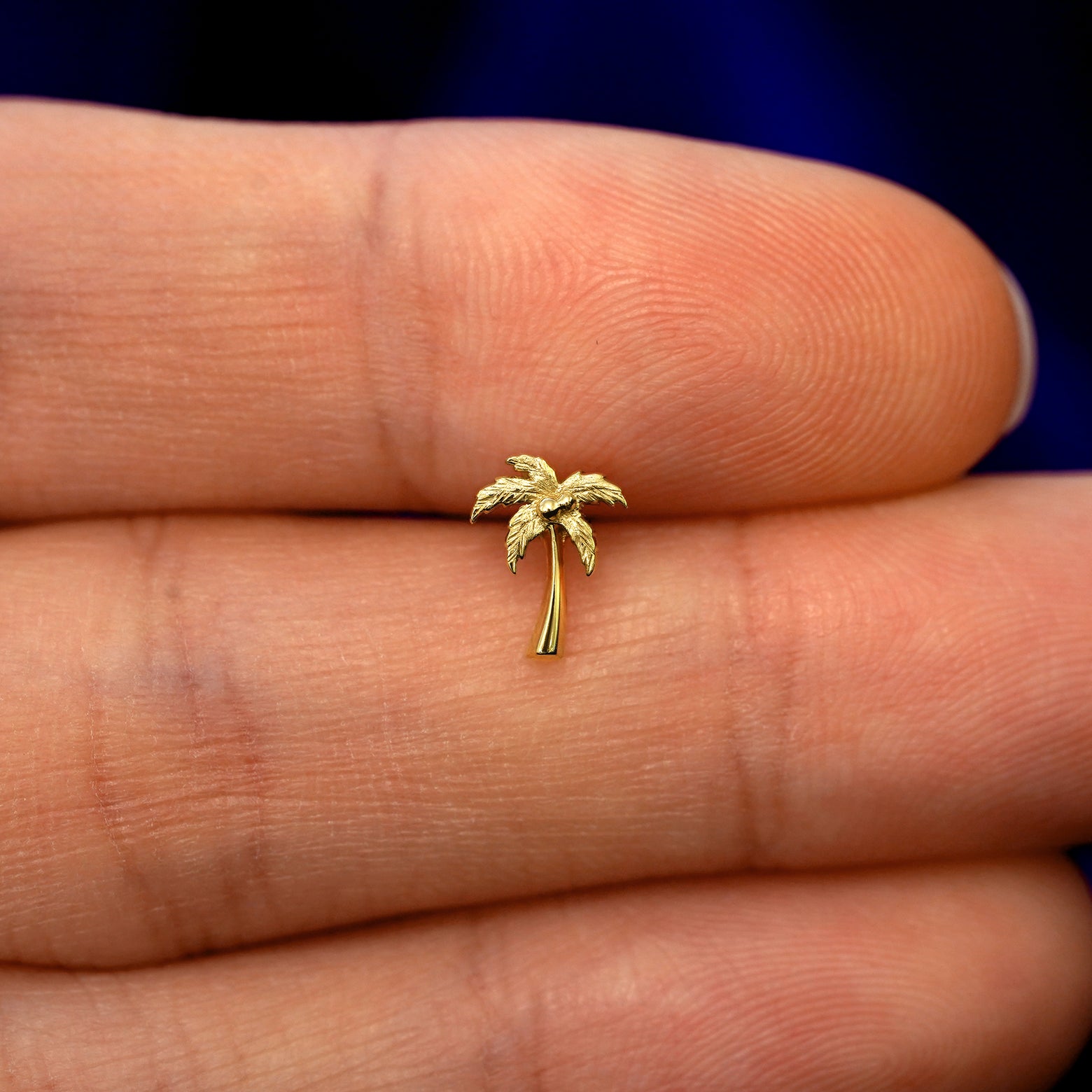 A model holding a solid gold Palm Tree stud earring between two fingers