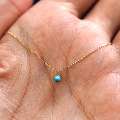 A solid 14k gold Turquoise Necklace resting in a models palm