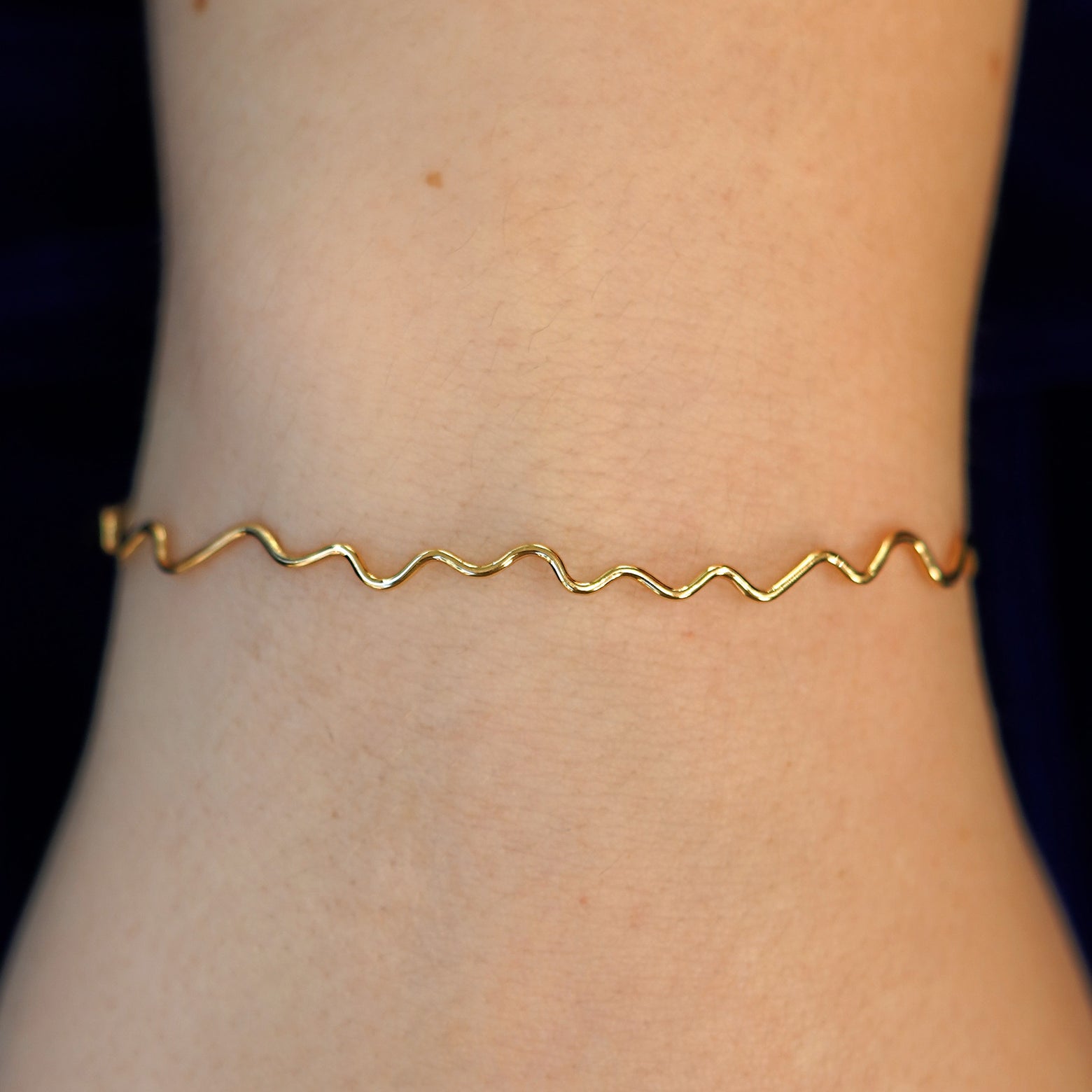A model's wrist wearing a 14k gold Wave Bangle Bracelet