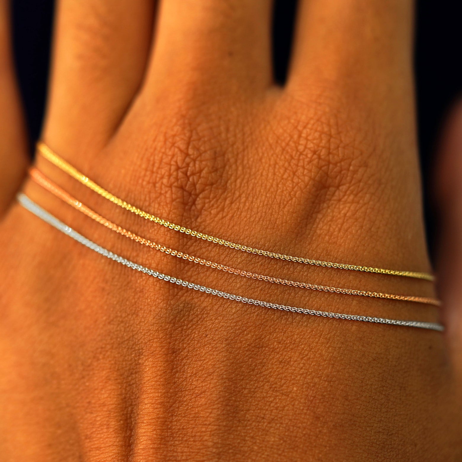 Close up view of a model's hand wearing three versions of the Wheat Bracelet in yellow, rose, and white gold
