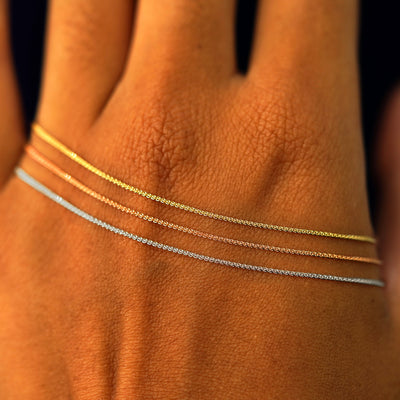 Close up view of a model's hand wearing three versions of the Wheat Bracelet in yellow, rose, and white gold