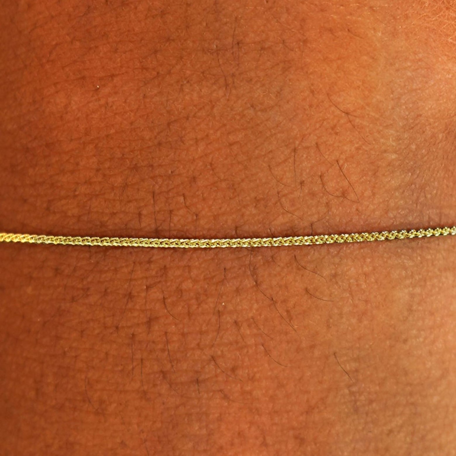 Close up view of a model's wrist wearing a solid 14k yellow gold Wheat Chain