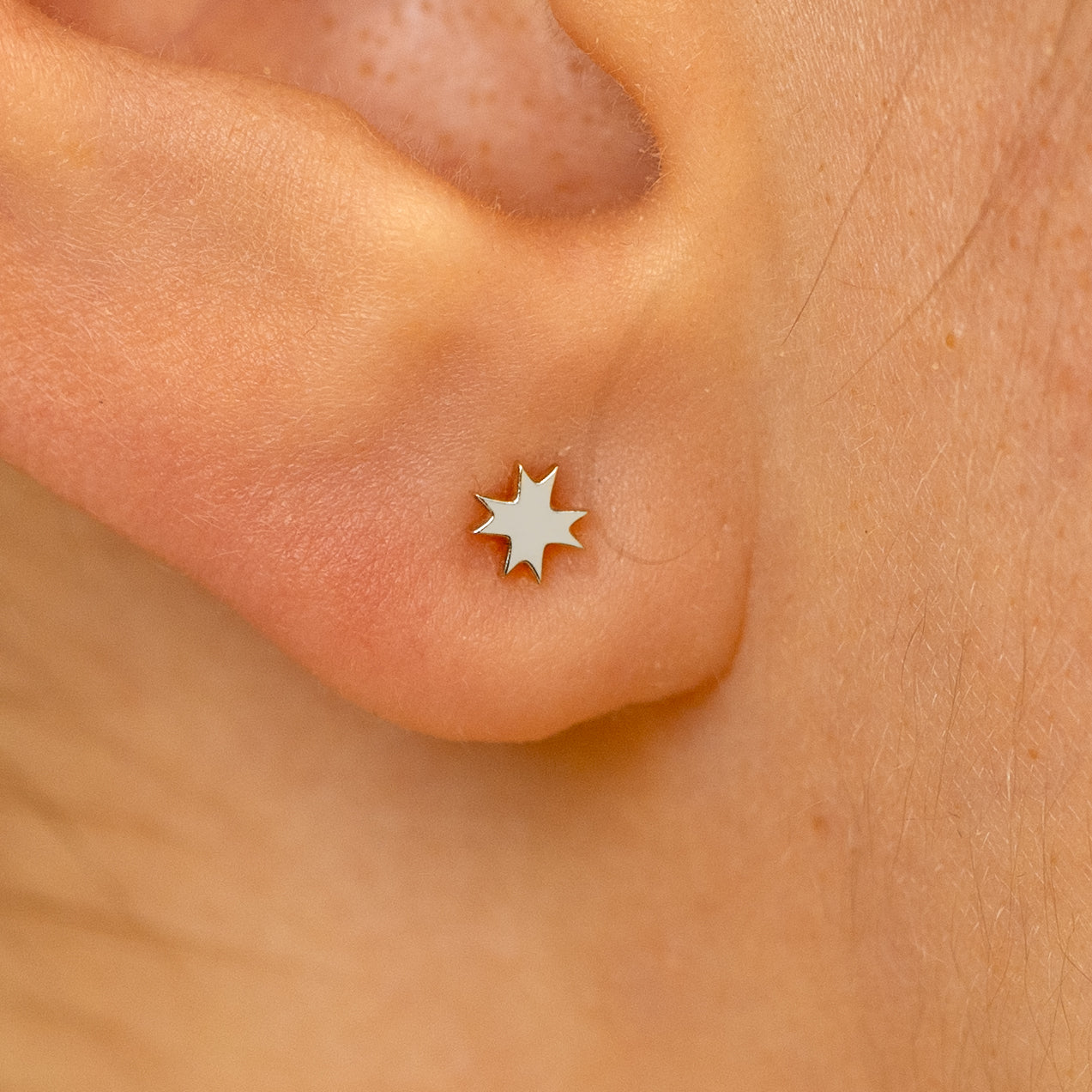 Close up view of a models ear wearing a 14k white gold 8 pointed star flatback piercing