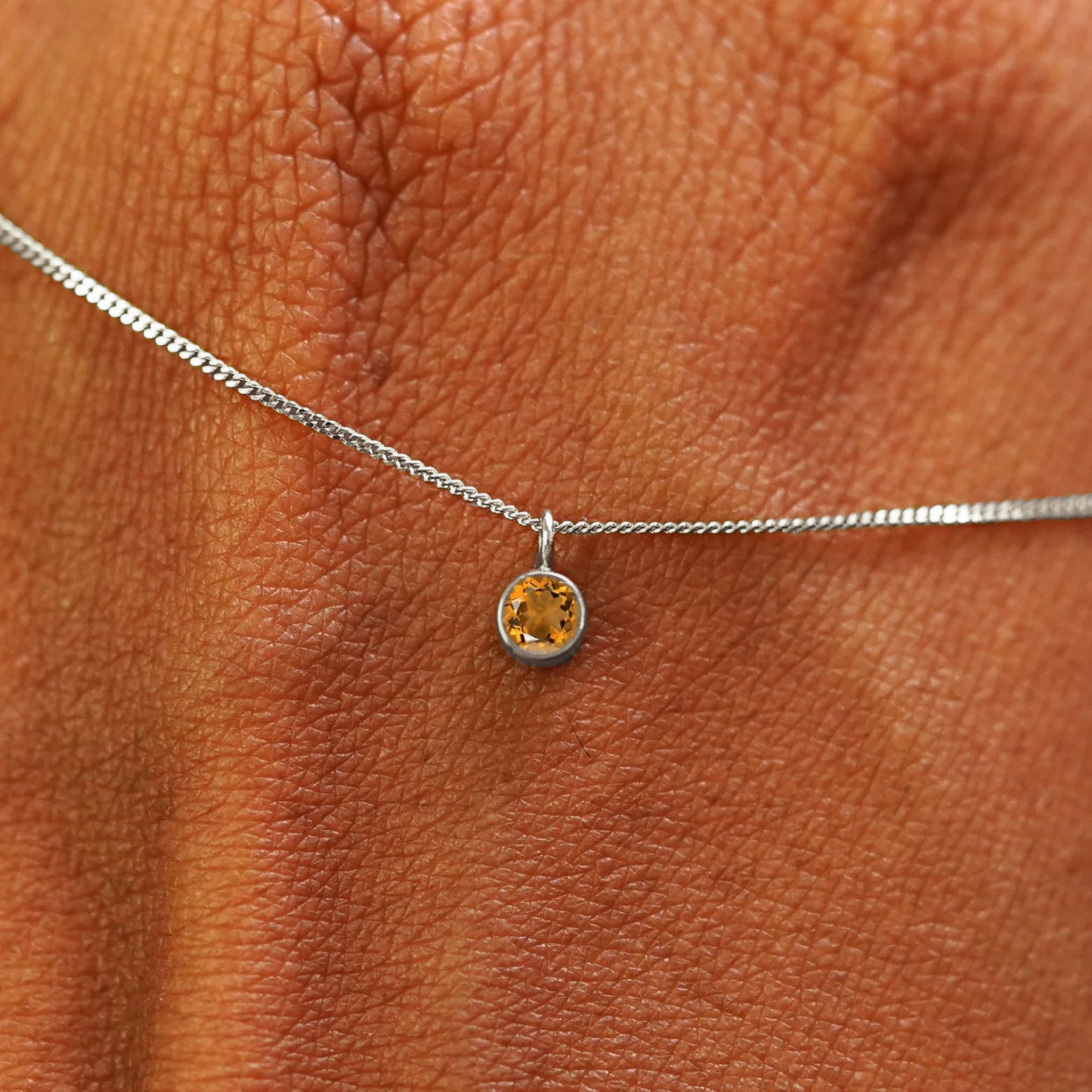 Close up view of a 14k white gold Citrine Necklace draped across the back of a model's hand