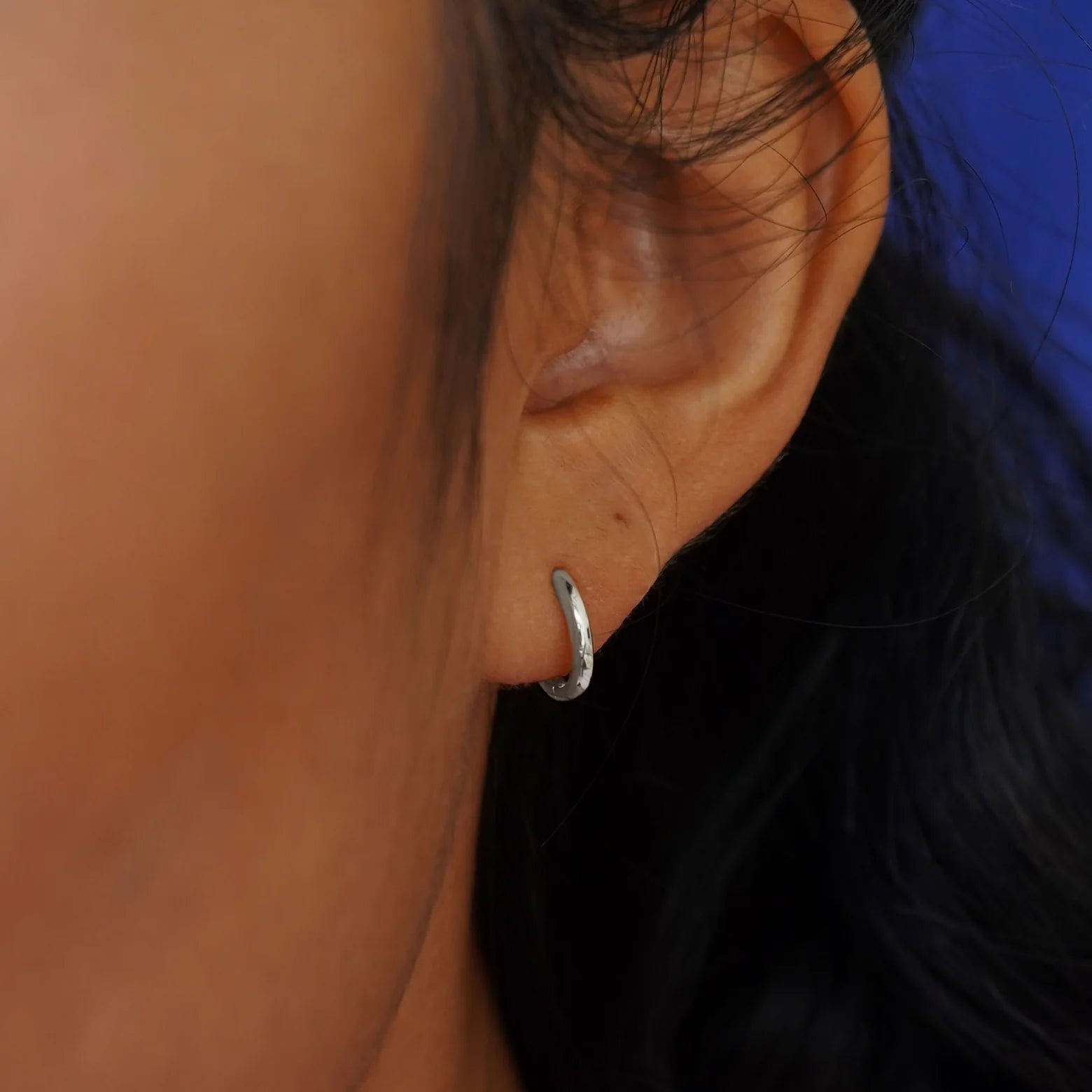 Close up view of a model's ear wearing a white gold Small Curvy Huggie Hoop
