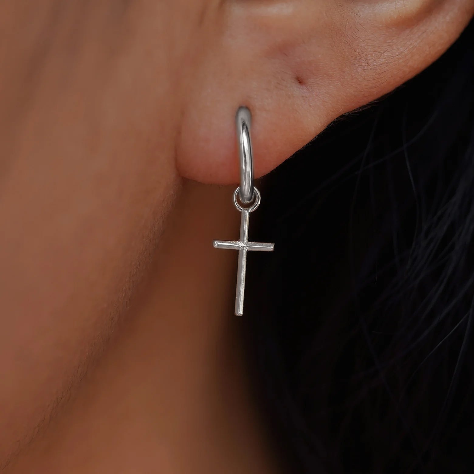Close up view of a model's ear wearing a white gold Cross Charm on a Curvy Huggie Hoop