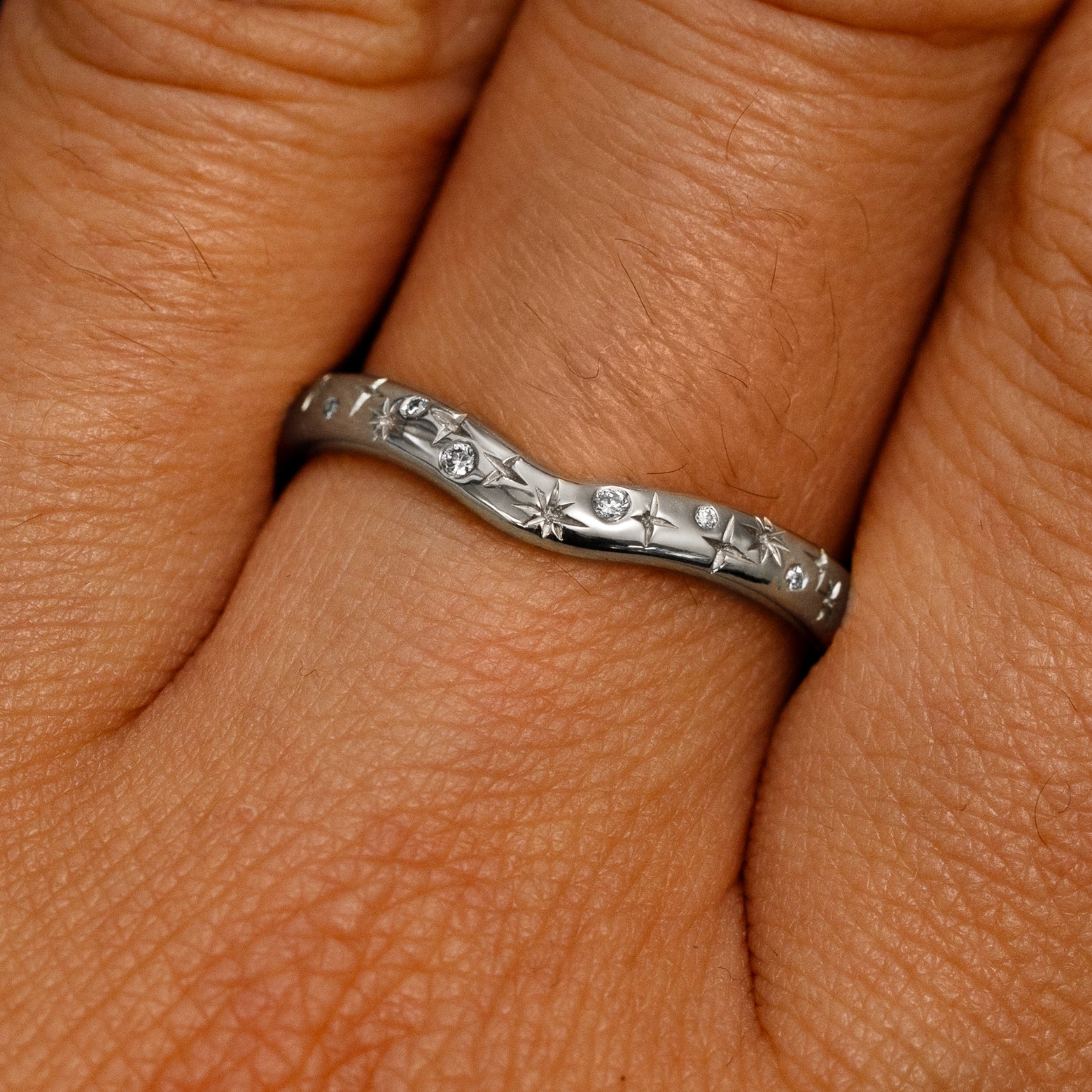 Close up view of a model's fingers wearing a 14k white gold Curvy Chevron Diamond Stars Band