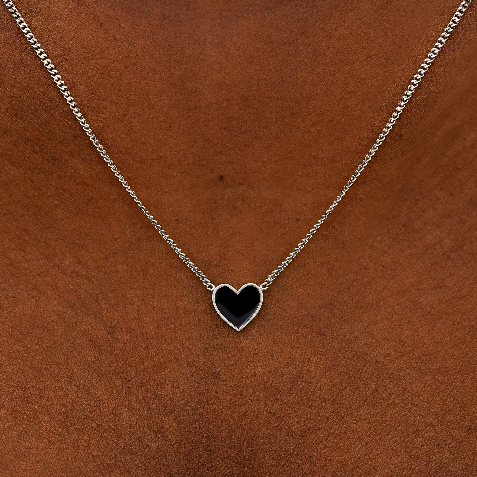Close up view of a model's neck wearing a white gold black enamel heart necklace