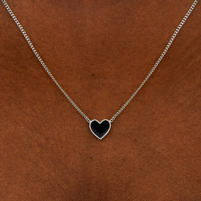 Close up view of a model's neck wearing a white gold black enamel heart necklace